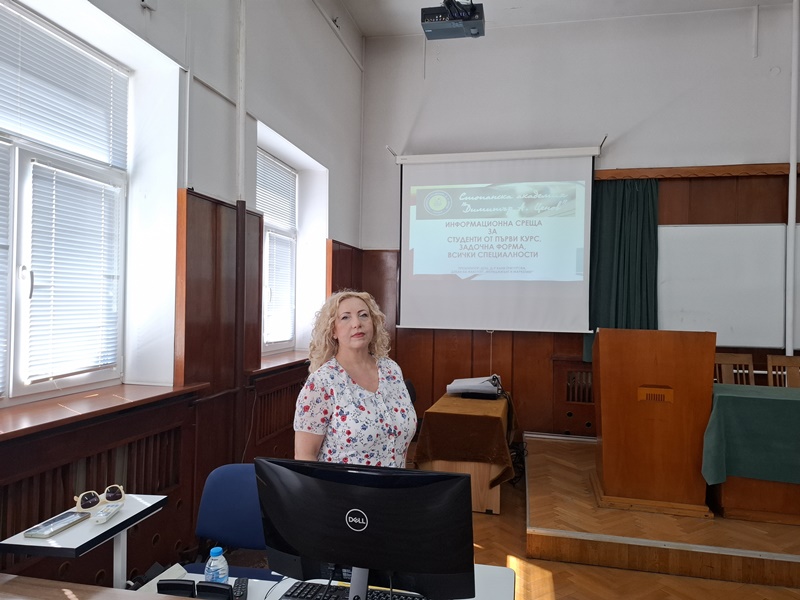 Доцент Григорова представя информация на първокурсниците в задочна форма пред компютър и бяла дъска