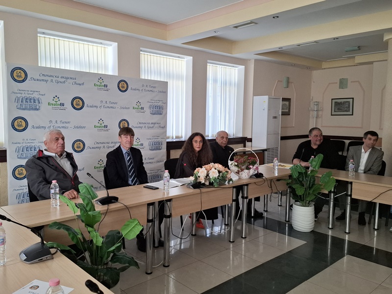 Участници в конференцията по случай 90 години счетоводно образование в Стопанска академия "Д.А. Ценов" - Свищов седящи около маса пред банер с логото на академията
