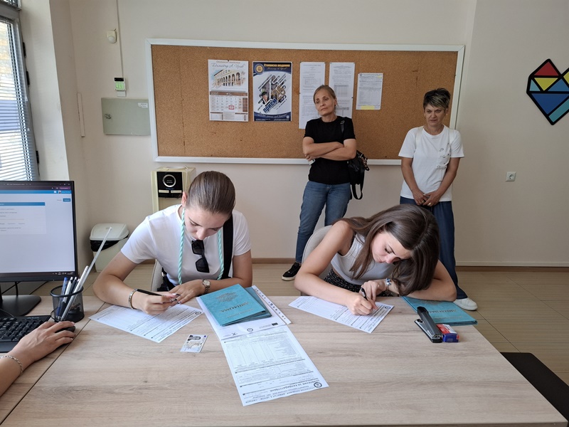 Записващи се студенти и служители обсъждат документи в приемната на академията