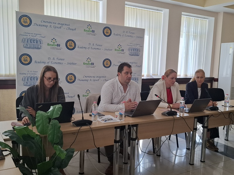 Участници дискутират по време на кръглата маса около маса покрита с материали и лога на проекта
