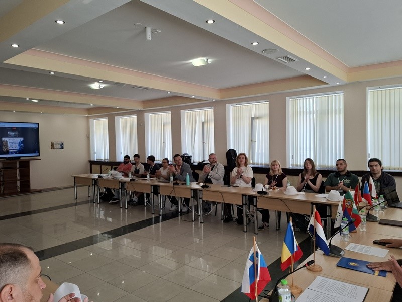 A group of people sitting at long tables in a room with flags AI-generated content may be incorrect.